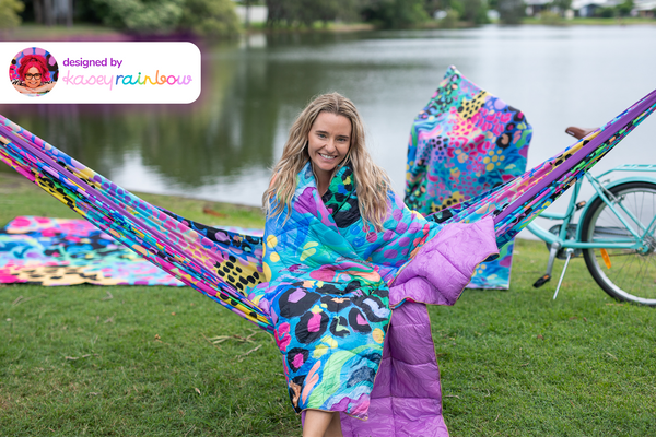 Recycled hammock with vibrant multicolor abstract print, purple accents, displayed outdoors by water with straps visible.