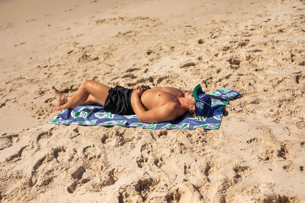 Warriors NRL recycled sand-free beach towel in navy with green and white geometric pattern, laid on sand