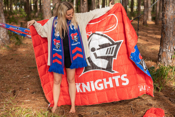 Red Knights NRL puffy blanket with knight logo and white text, displayed outdoors with matching blue scarf