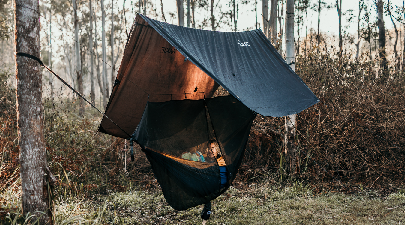 Person snug in nakie Hammock protected by a Nakie Rain tarp in the woods.
