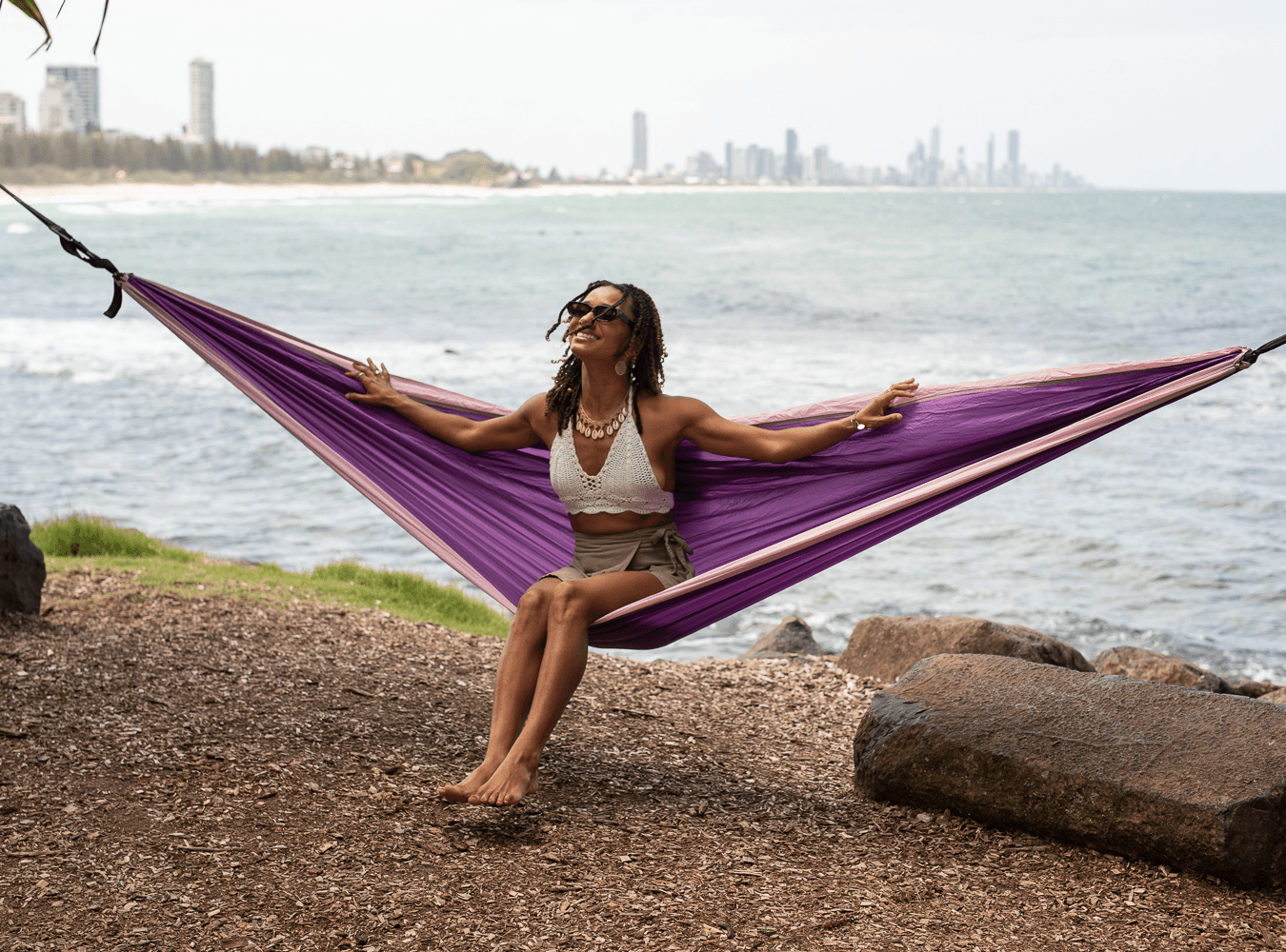 Woman relaxing in purple recycled hammock by the beach