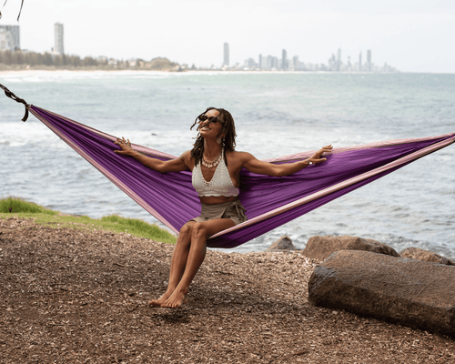 Woman relaxing in purple recycled hammock by the beach