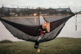Woman in a Nakie hammock with a bugnet relaxing by the water. Nakie - Australia