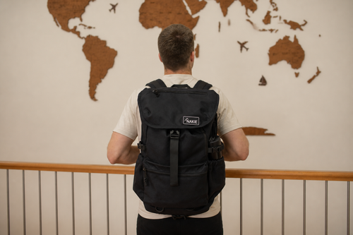 Black recycled travel backpack with flap closure, side pockets, and branded label, worn on back view.