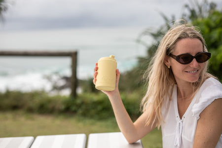 Woman holding a Daisy Yellow Cooler & Coffee Cup by the ocean