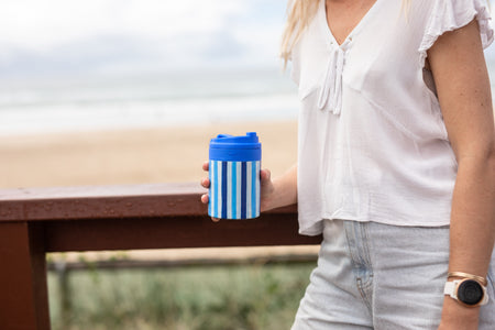 Ocean Breeze Cooler & Coffee Cup held on a beach boardwalk