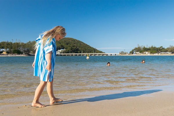 Kids hooded towel in blue and white stripes, worn by child on beach with ocean background