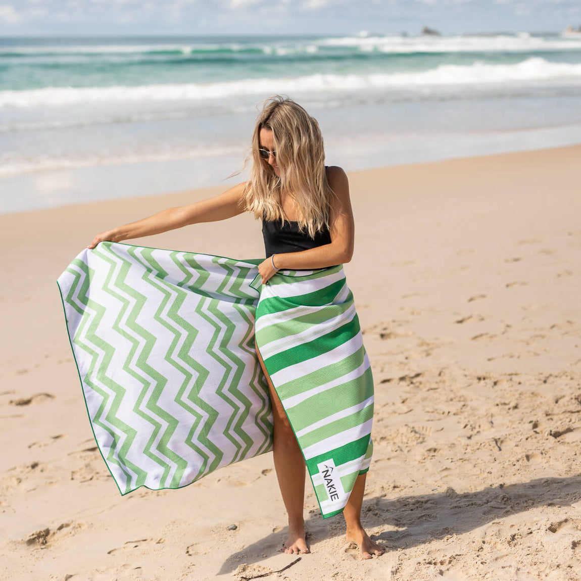 Green and white chevron recycled beach towel with striped wrap, displayed on sandy beach