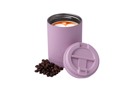 Dusty pink insulated coffee tumbler with black lid, filled with latte art, shown with matching lid and coffee beans.