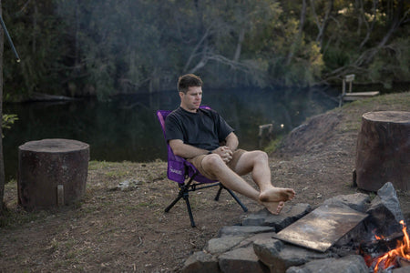 Man with his feet up in the Mulberry Purple camping chair by a campfire