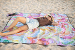 Recycled picnic blanket with multicolour watercolour abstract print, displayed on sand with black binding edges. preview #8