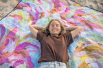 Recycled picnic blanket with colorful watercolor abstract pattern in magenta, blue, yellow, and orange tones on sand. preview #4