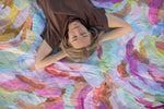 Recycled picnic blanket in multicolor watercolor floral print, displayed overhead with woman lying on it. preview #9