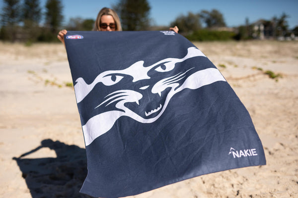 Navy beach towel with white striped Geelong Cats AFL logo design, sand-free fabric, held on sandy beach