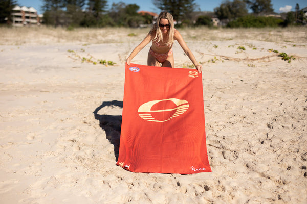 Gold Coast SUNS recycled sand-free beach towel in red with cream logo, displayed on beach.