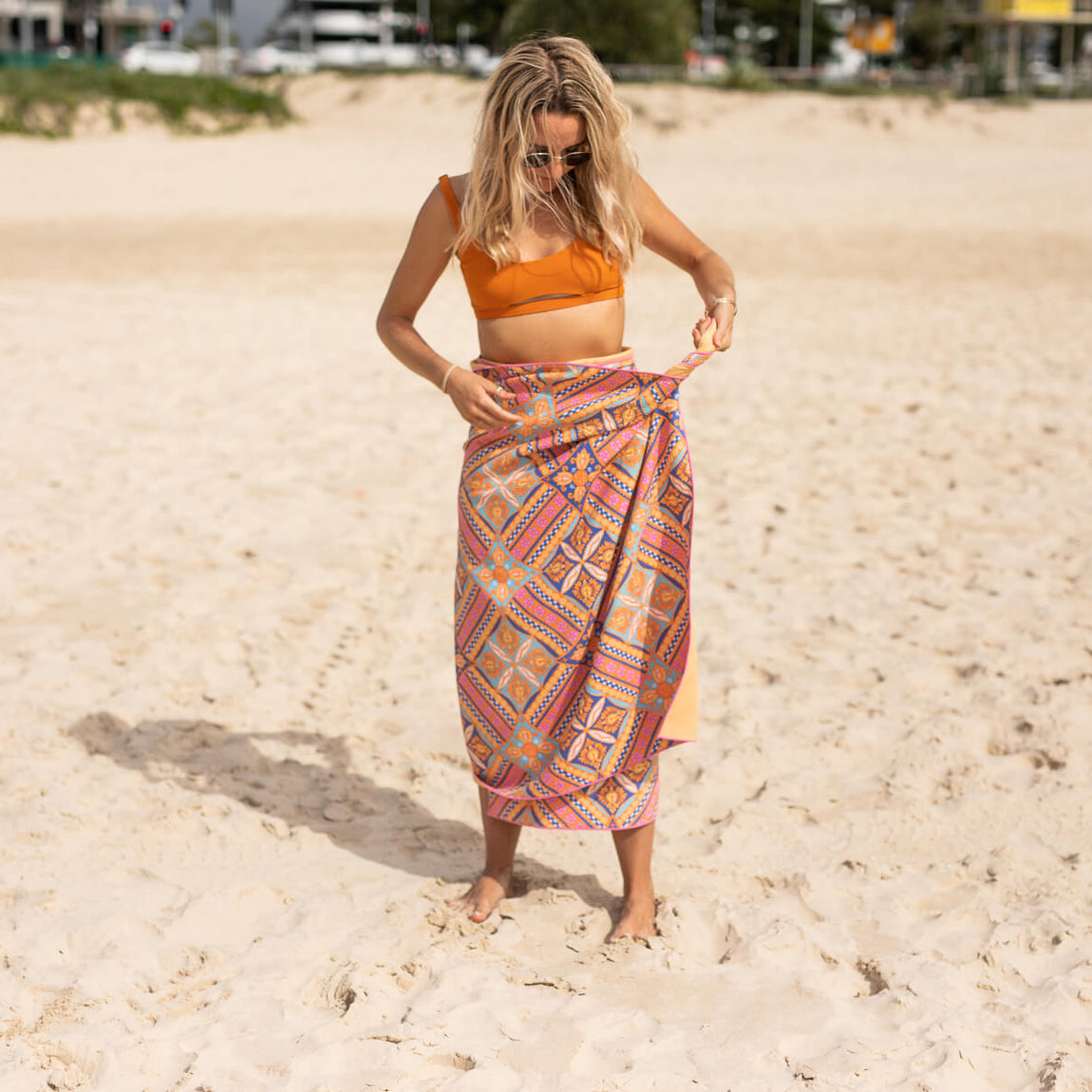 Recycled sand-free beach towel in coral geometric print, worn as wrap on beach