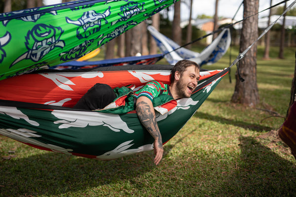 Rabbitohs red and green recycled fabric hammock with white graphic design, suspended between trees.