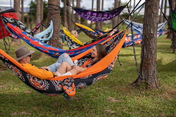 Orange and black patterned recycled hammock with straps, suspended between trees in outdoor setting.