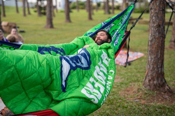 Green quilted hammock with navy Raiders NRL logo, suspended between trees in outdoor setting
