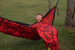 Man smiling in a red NRL Dragons Nakie hammock with black patterns on grass preview #3