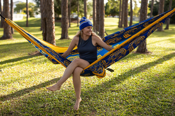 Blue and gold patterned recycled hammock with straps, person relaxed in hammock between trees in park setting