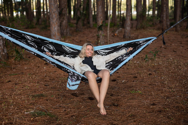 Blue and black leaf-patterned recycled hammock with integrated straps, suspended between trees.