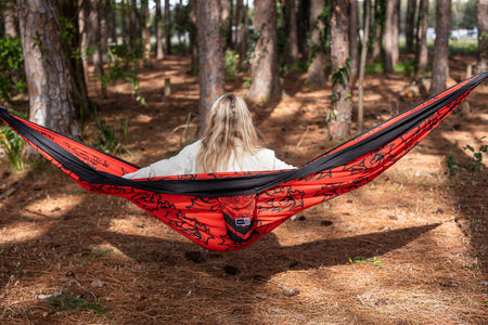 Person sitting in a red and black Nakie NRL Dragons hammock in a forest setting