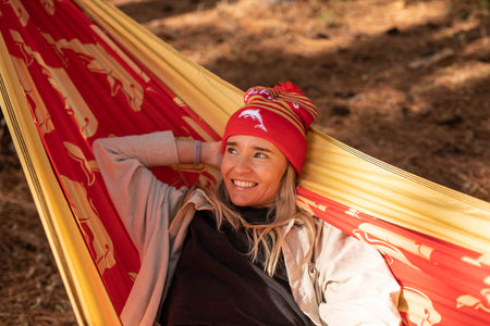 WOman lying in a red and gold Nakie NRL Dolphins hammock with a outdoor background