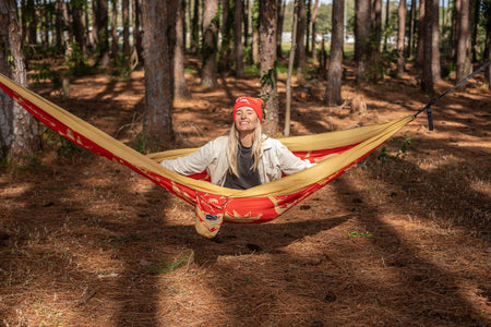 Happy woman sitting in Nakie NRL Dolphins Hammock in the forest.