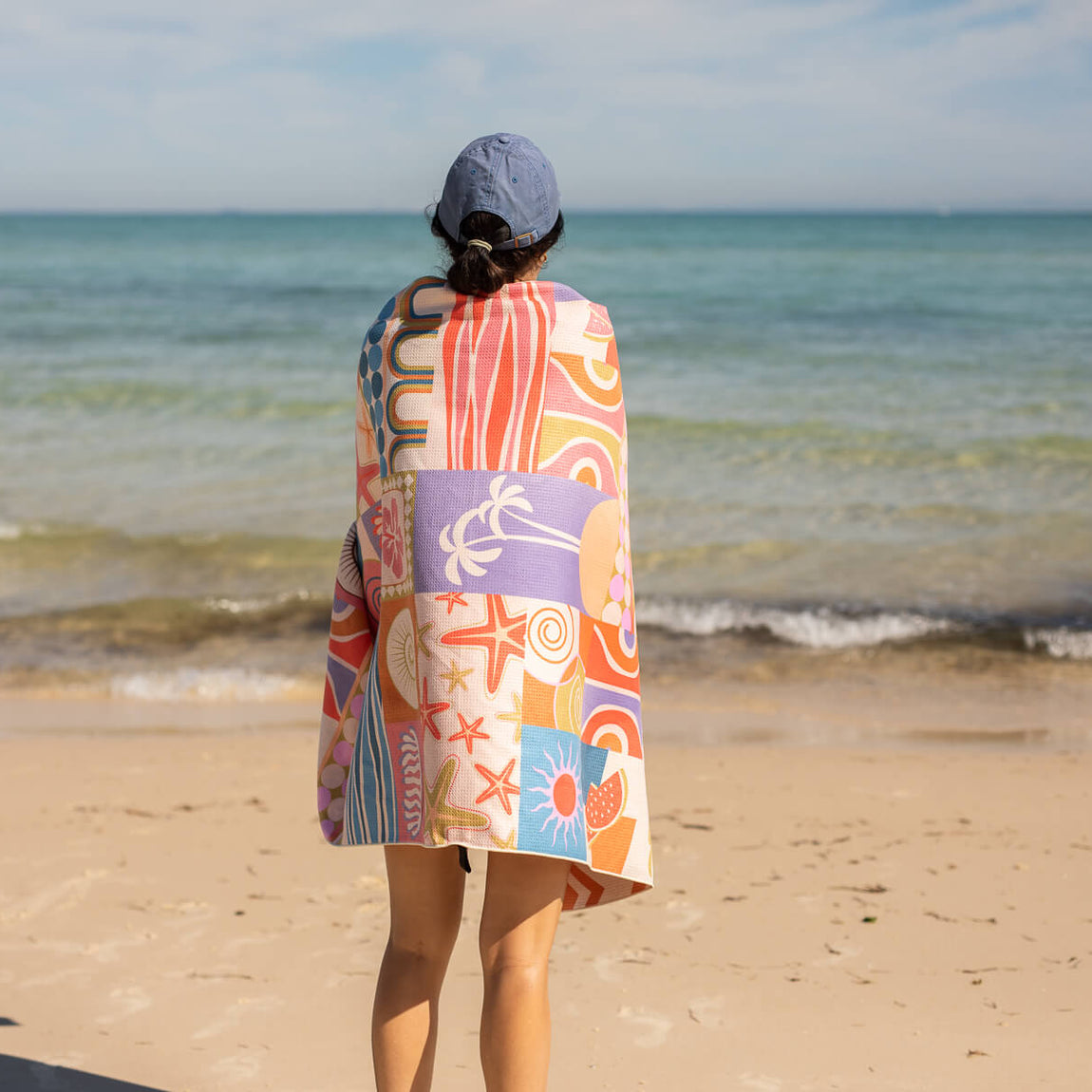 Recycled sand-free beach towel with retro multicolour coastal print, worn over shoulders at beach