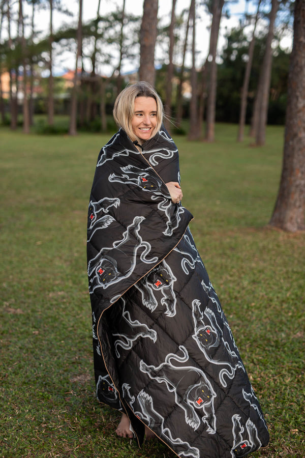 Black puffy blanket with white snake and red badge pattern, wrapped around woman outdoors