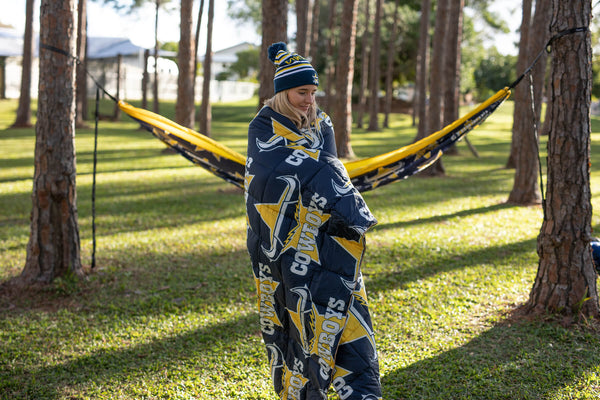 Cowboys navy and gold patterned sustainable down puffy blanket draped over person in hammock