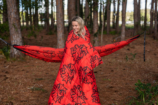 Red quilted puffy blanket with black dragon pattern, worn as cape outdoors in forest setting