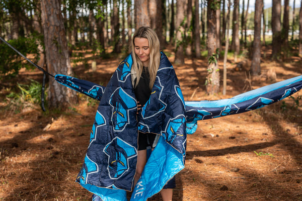 Navy and blue geometric patterned puffy blanket with bright blue lining, draped around person in forest setting