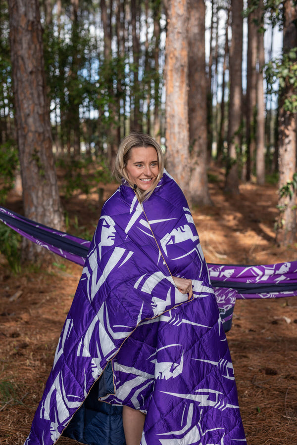 Purple and white geometric patterned sustainable down puffy blanket draped around woman in forest setting