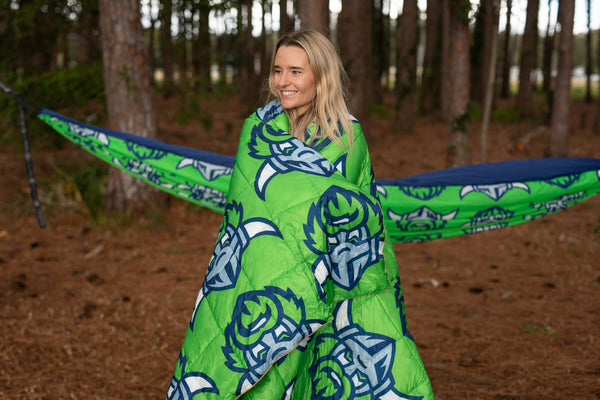 Green Raiders puffy blanket with navy tribal design, worn as wrap outdoors in forest setting.