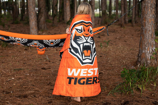 Orange NRL Tigers puffy blanket with tiger face graphic and West Tigers text, worn as cape outdoors.