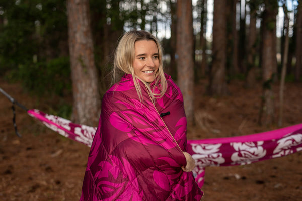 Magenta quilted down puffy blanket wrapped around person in forest setting