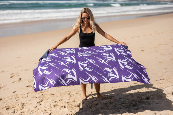 Purple sailboat-print recycled sand-free beach towel held open by woman on beach