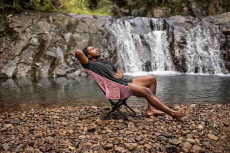 Man reclining in the Rosy Tides Camping Chair at a waterfall