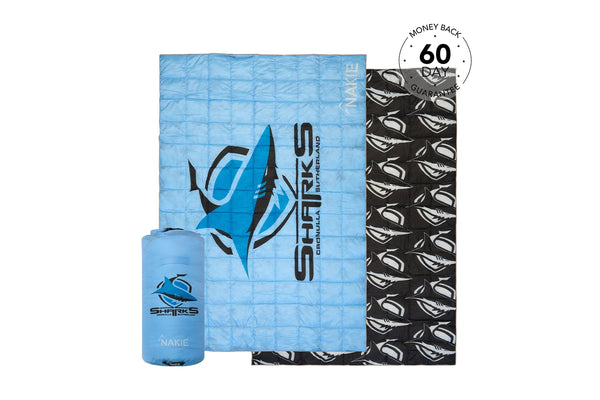 Blue quilted puffy blanket with shark graphic and black patterned reverse side, shown with compression pouch