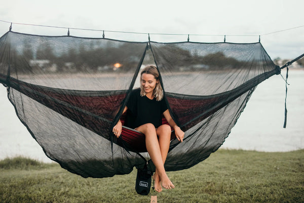 Recycled hammock with integrated bug net in black and burgundy, suspended between trees with person seated inside