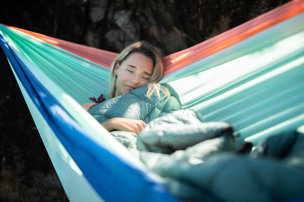 Woman relaxing in rainbow-striped recycled hammock with mint green puffy blanket and towel